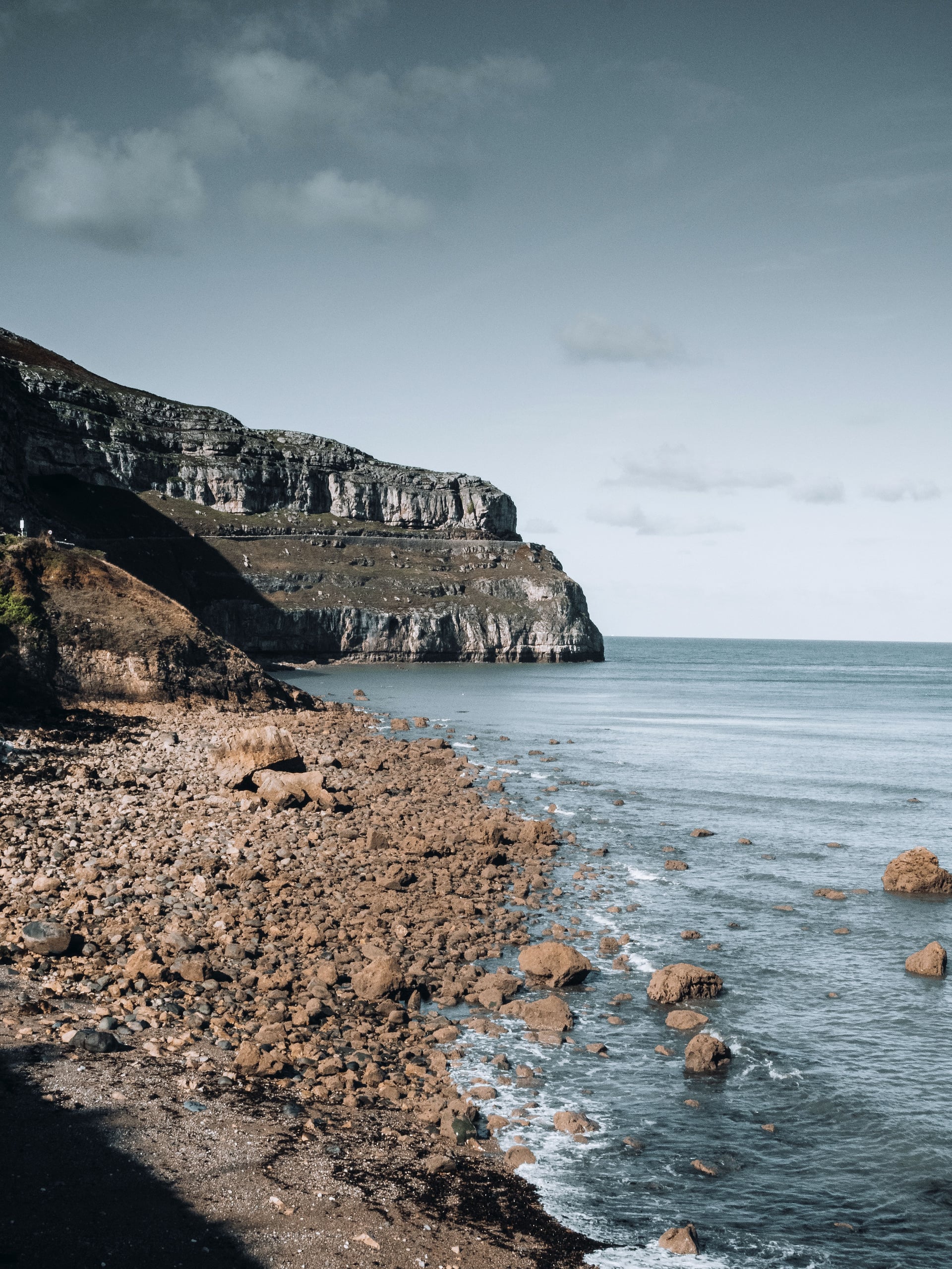 Rocky shoreline with dramatic limestone cliffs dropping to a calm grey-blue sea on the North Wales coastline