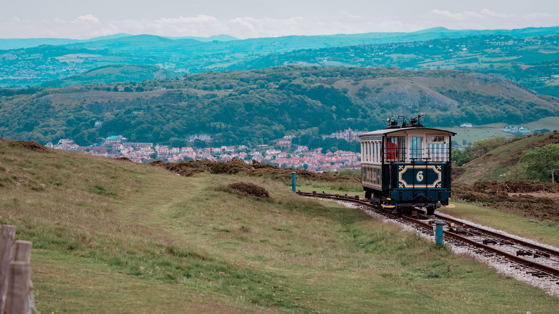 Great Orme Tramway car number 6 climbing the hillside above Llandudno, with the town's rooftops and rolling Welsh hills stre…