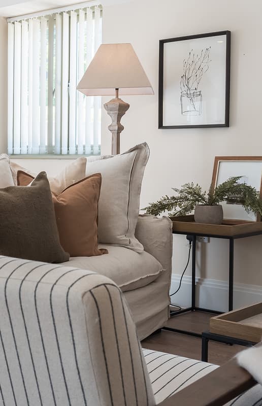 Neutral-toned living room corner with linen sofa, layered cushions, wooden floor lamp, and botanical wall art at Pittern Hil…