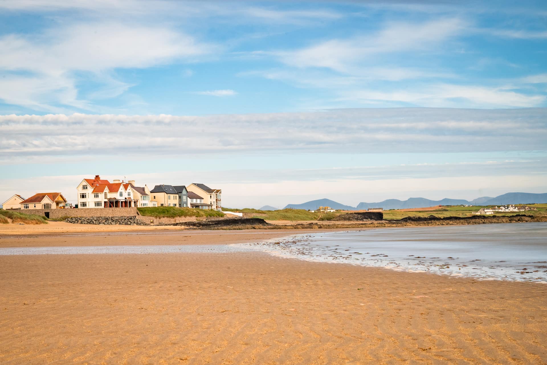 Wide sandy beach at Rhosneigr, Anglesey, with coastal holiday homes and the Snowdonia mountains visible on the horizon