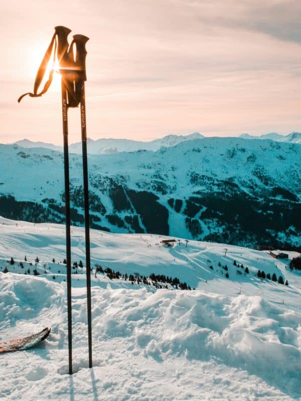 Ski poles planted in fresh powder snow overlooking alpine slopes and mountain peaks at golden hour