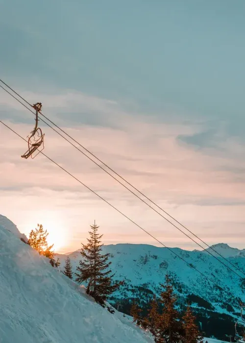 Chairlift ascending snowy mountain slopes at sunset with pink and blue alpine sky, perfect for luxury ski chalet holidays