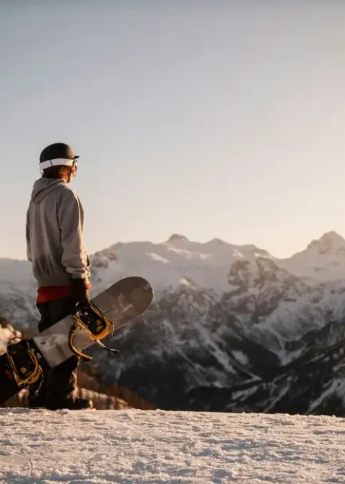 Snowboarder overlooking snow-capped mountain peaks at golden hour, perfect for alpine chalet guests seeking winter sports ad…
