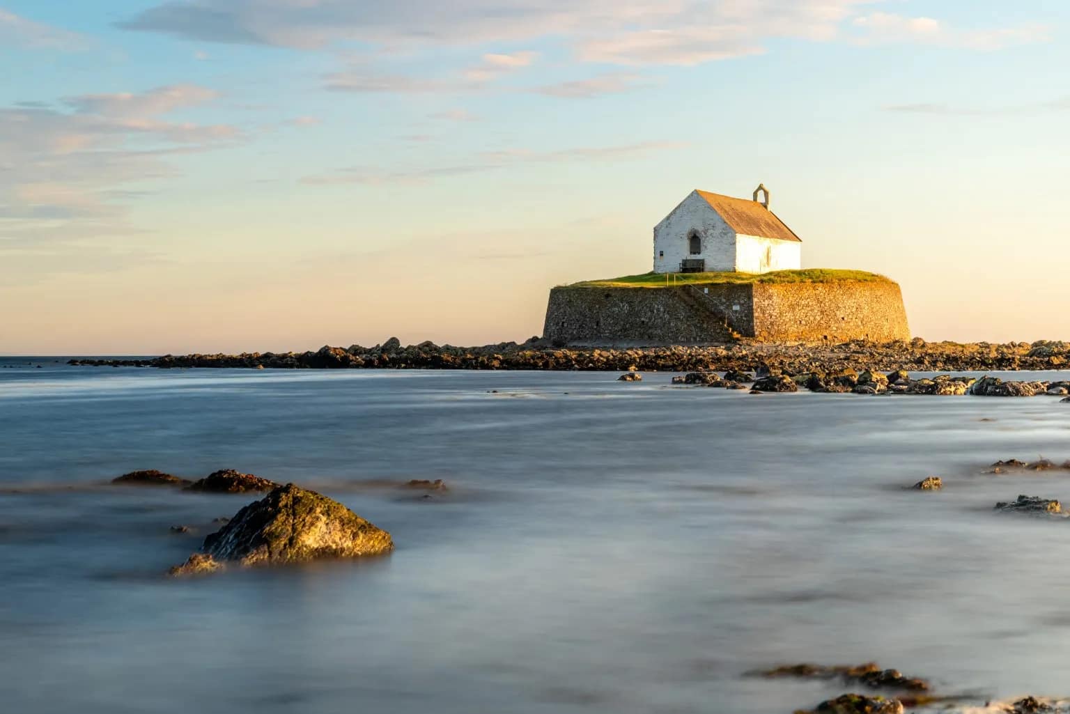 St Cwyfan's Church perched on a rocky tidal island off Anglesey at golden hour, with silky long-exposure sea surrounding the…