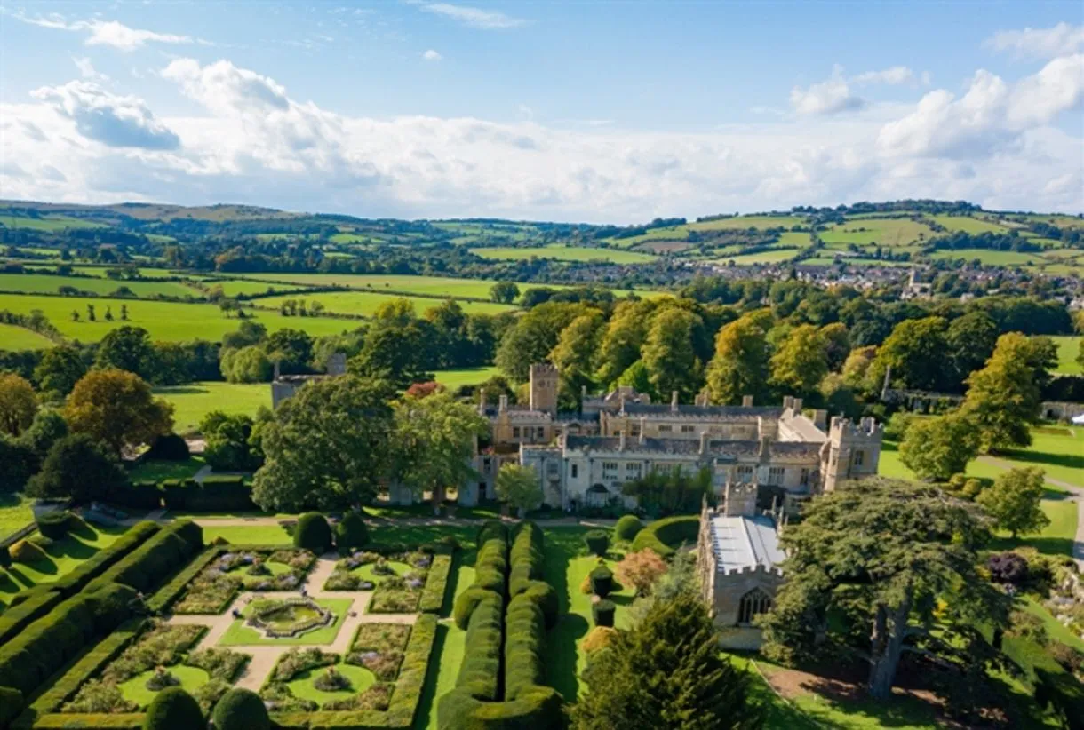 Aerial view of Sudeley Castle with formal parterre gardens, chapel, and sweeping Cotswolds countryside beyond