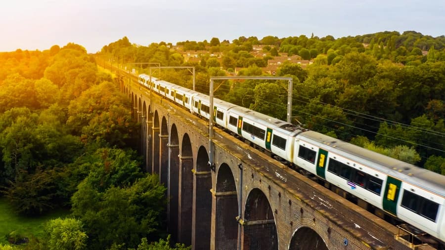 Southern rail train crossing a Victorian brick viaduct surrounded by lush green woodland at golden hour in the English count…