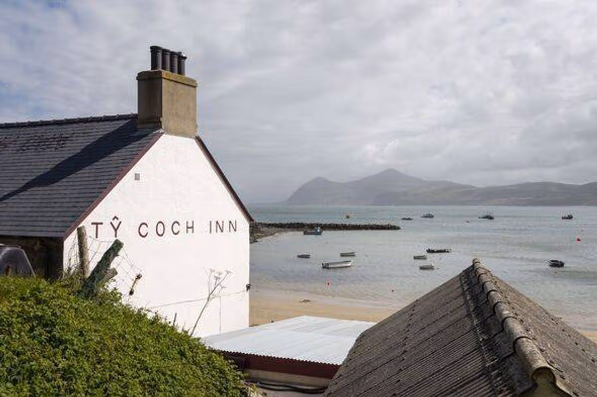 Tŷ Coch Inn at Porthdinllaen on the Llŷn Peninsula, with small boats moored in the sandy bay and mountains beyond