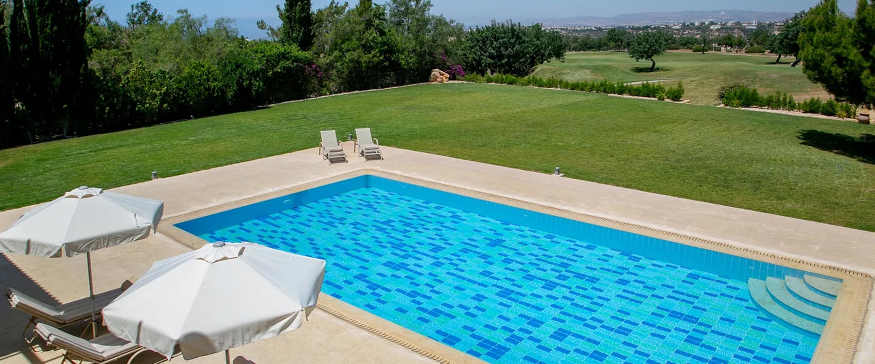Private pool with mosaic tiles and sun loungers overlooking a golf course and distant coastline on a sunny day