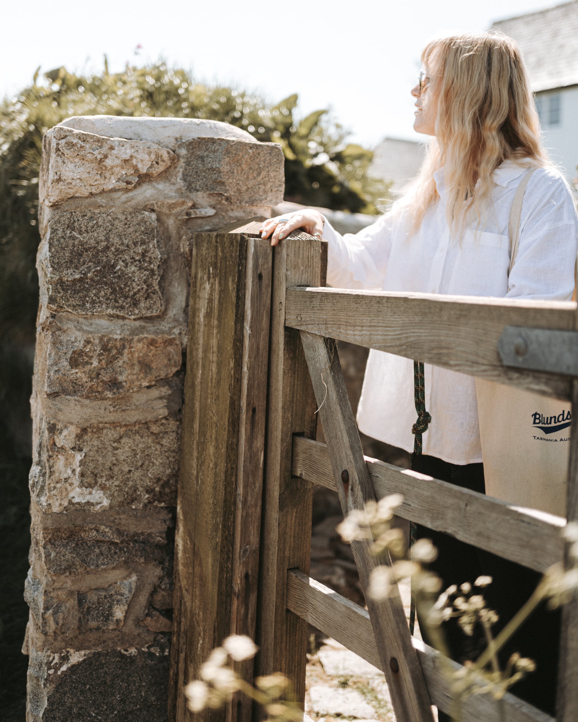 Woman leaning on a rustic wooden gate beside a granite stone wall, enjoying the sunny countryside surroundings on a UK holid…