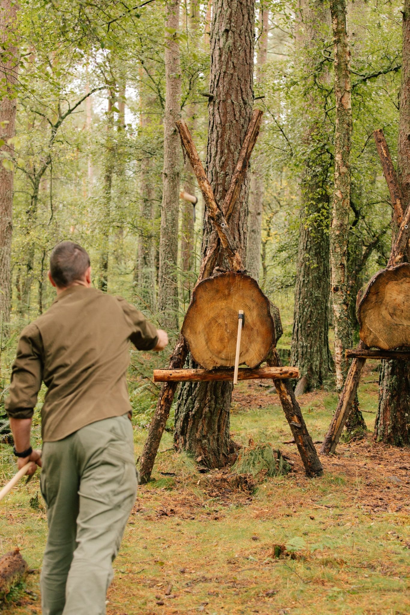 Guest throwing an axe at a rustic log target during an outdoor woodland activity experience