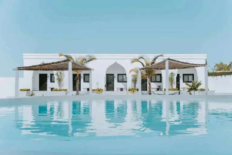 White Mediterranean villa with infinity pool reflecting the building, featuring palm trees and covered terraces