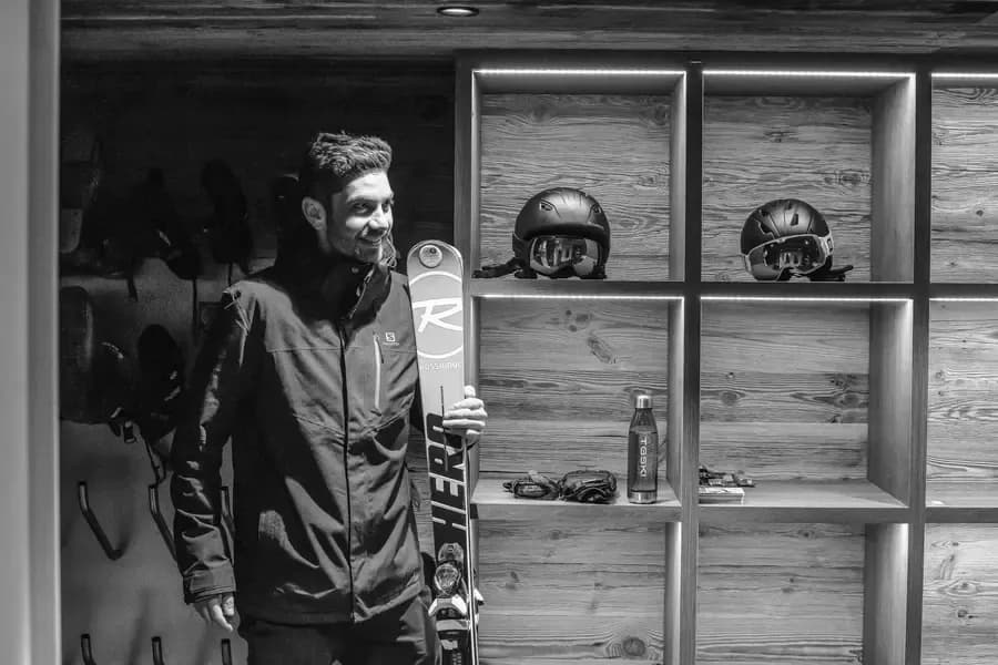 Guest preparing skis in chalet boot room with wooden storage cubbies for helmets and equipment