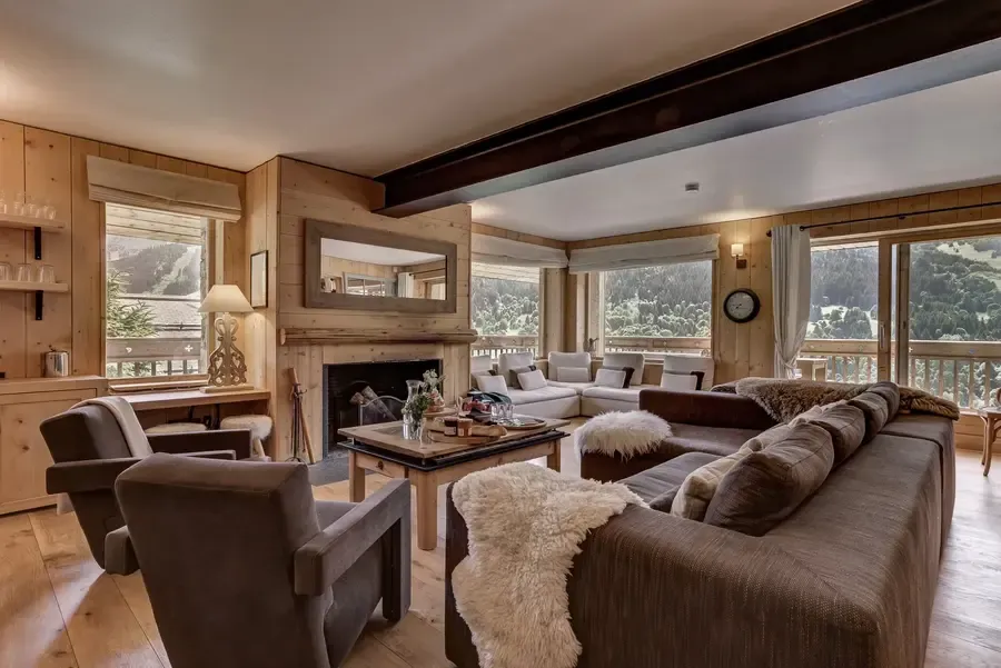 Luxury alpine chalet living room with exposed beams, stone fireplace, plush sofas and panoramic mountain views