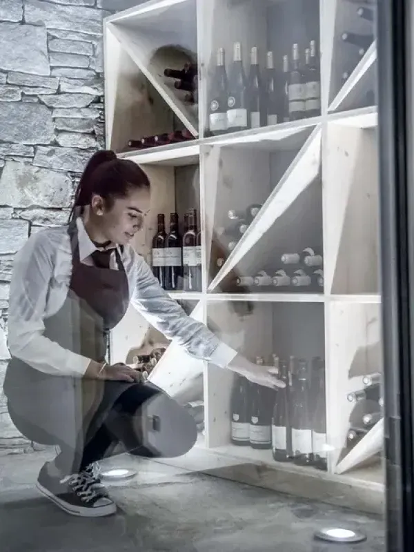 Staff member selecting wine from modern white wine cellar with stone wall feature in luxury holiday property